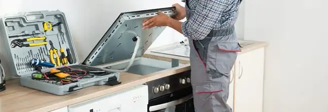 Cooktop repair technician lifting a built-in stovetop for service in Lakewood, CO