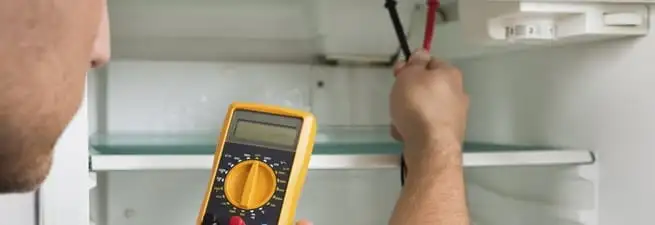 Refrigerator repair technician testing electrical components with a multimeter in Lakewood, CO
