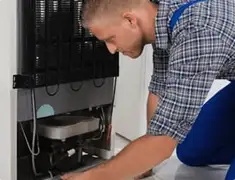 Refrigerator repair technician servicing the compressor and condenser area in Lakewood, CO