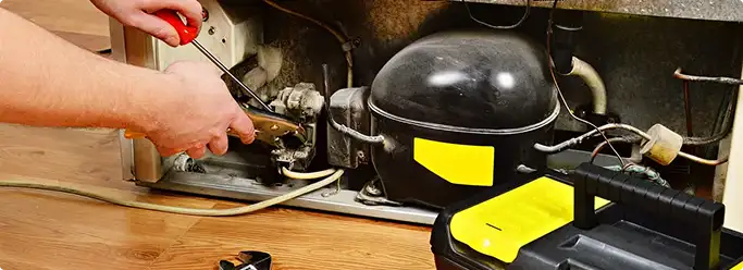 Refrigerator repair technician fixing the compressor and wiring in Lakewood, CO